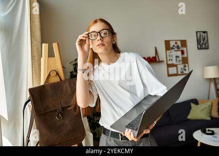 A young man in glasses looks up from his laptop, deep in thought in a cozy setting. Stock Photo