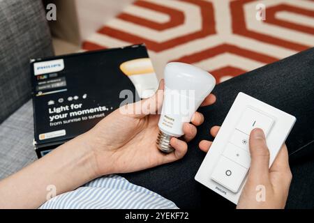 Paris, France - Aug 16, 2029: Person holding a Philips Hue smart light bulb and remote control, highlighting adjustable lighting options for home ambiance and smart home setups Stock Photo