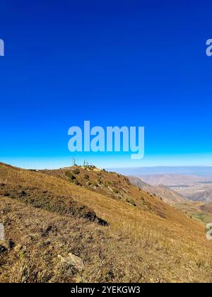 A mountain station on the ridge under a clear blue sky in Kyrgyzstan, with snowy slopes and hills in the background Stock Photo