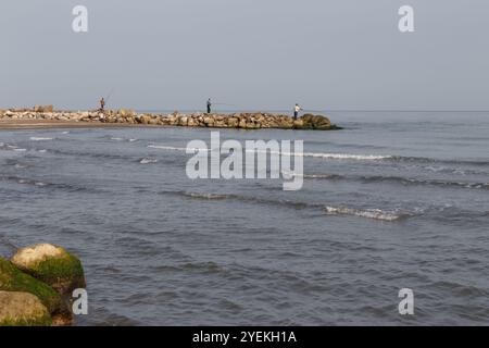 Fishermen stand on the shore and catch fish with a fishing rod. Caspian Sea, Iran Stock Photo