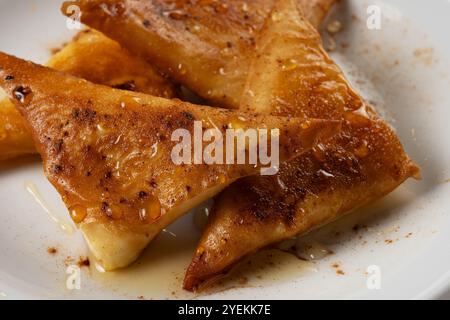 Mini cheese pies with myzithra, cretan honey and cinnamon on white plate. Stock Photo