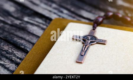 Dark red copper cross leaning against an old open book symbolizing the spread of Jesus Christs love among Christians reflecting faith devotion and the Stock Photo