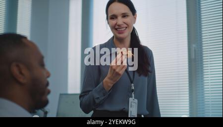 Team of diverse technical customer support specialists talk, eat pizza delivery for dinner. Two multiethnic company employees take a break in modern bright call center office equipped with computers. Stock Photo