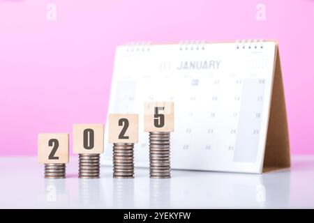 Stack of coins beside a wooden block labeled '2025' and a calendar. Symbolizes financial planning for the upcoming year, emphasizing budgeting and set Stock Photo
