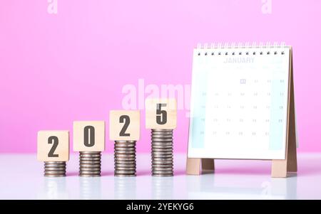 Stack of coins beside a wooden block labeled '2025' and a calendar. Symbolizes financial planning for the upcoming year, emphasizing budgeting and set Stock Photo