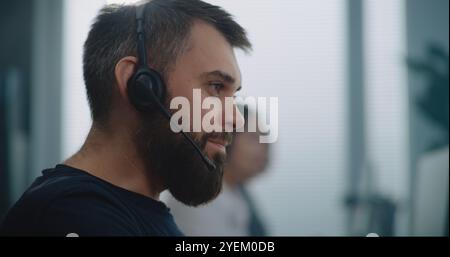 Modern call center office: Close up portrait of Caucasian technical support specialist in headset communicating with client on call, providing online assistance. Customer experience officer working. Stock Photo