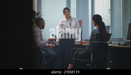 Team of diverse company employees talk and eat pizza delivery for lunch. Group of technical support operators having break from work in modern and bright call center office equipped with computers. Stock Photo