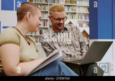 Two people sitting in study space working together on a laptop. Engaging in discussion and exchanging notes in a library setting Stock Photo