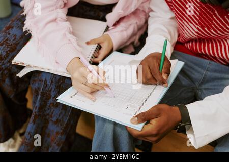 Close-up showing hands of students holding pencils and writing on paper together in study session. Students seem focused and engaged while working on schoolwork Stock Photo