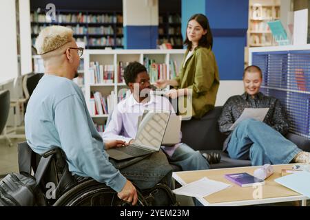 Group of diverse students collaborating in university library, sharing ideas and working on projects amidst bookshelves and resources. Engaging in productive study session Stock Photo