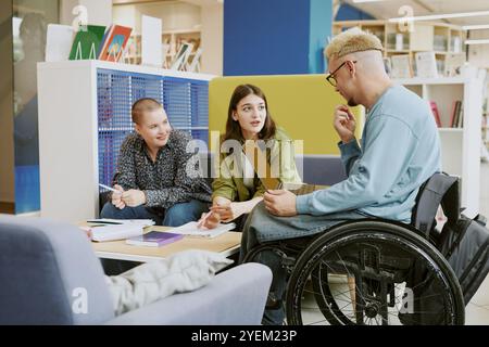 Group of students brainstorming ideas and discussing projects during study session in modern library with shelves of books and various seating arrangements surrounding them Stock Photo