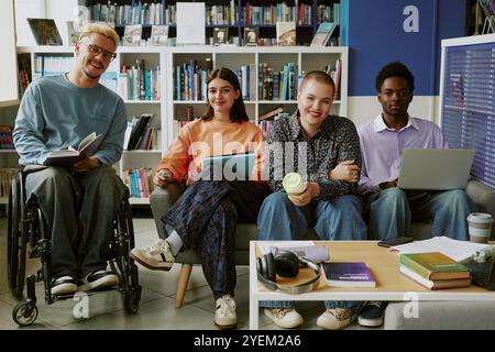 Group of diverse young adults enjoying time in library while discussing and working on projects. One member is in wheelchair, all appear engaged and happy Stock Photo