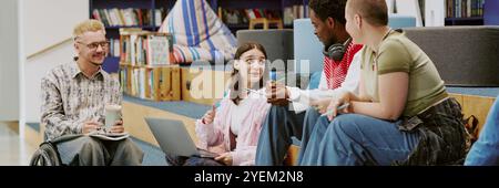 Group of students studying and discussing with laptops, notebooks, and pens in modern library environment. Multi-ethnic students engaged in learning together Stock Photo