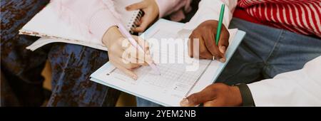 Two individuals engrossed in writing in notebook while participating in collaborative learning session. Hands are visibly working on accomplishing task without gaze towards camera Stock Photo