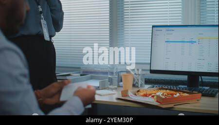 Team of diverse technical customer support specialists talk, eat pizza delivery for dinner. Two multiethnic company employees take a break in modern bright call center office equipped with computers. Stock Photo