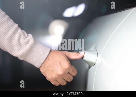 Man's hand touching the car door to unlock it without using a remote or key. Represents the concept of modern vehicle technology, highlighting keyless Stock Photo