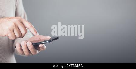A person casually holding a smartphone, engaging with the touch screen in a subtle motion. Grey background ann providing generous space for additional Stock Photo