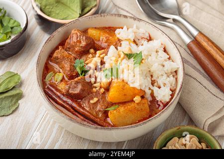 Bowl of delicious massaman curry with rice and peanuts on white wooden background, dish of thailand Stock Photo