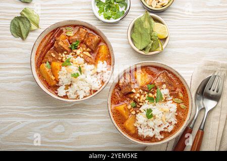 Two bowls of delicious massaman curry with beef, potatoes, rice, and peanuts, garnished with parsley on white wooden background, Thai cuisine Stock Photo
