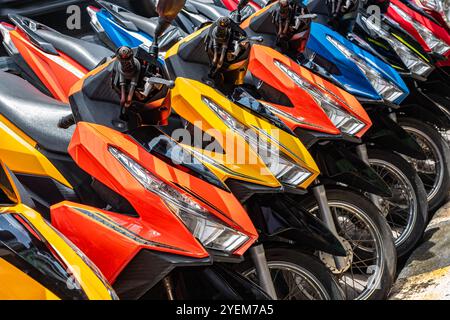 Motorcycles for rent or for sale on the city street. Lots of colorful scooters to ride. Motorbike, motorcycle scooters parked in row in city street. C Stock Photo