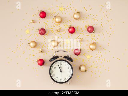 Old retro alarm clock with Christmas baubles, classic bells and golden glitter stars confetti on cream background. Minimal Christmas and New Year idea Stock Photo
