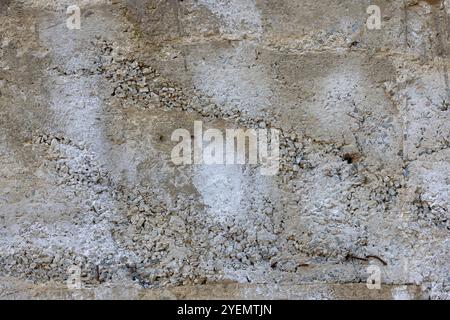 Cracked and Pebble-Embedded Concrete Wall, Weathered Stone Textured Surface, Rugged Architectural Element, Concrete Texture Concept. Stock Photo