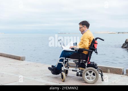 man sitting in wheelchair working on laptop Stock Photo