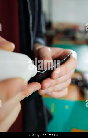 The hands of the master sew handmade leather products. Men's hands connect the parts, creating quality leather accessories. Working process in a leath Stock Photo