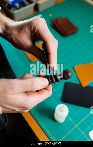 The hands of the master sew handmade leather products. Men's hands connect the parts, creating quality leather accessories. Working process in a leath Stock Photo