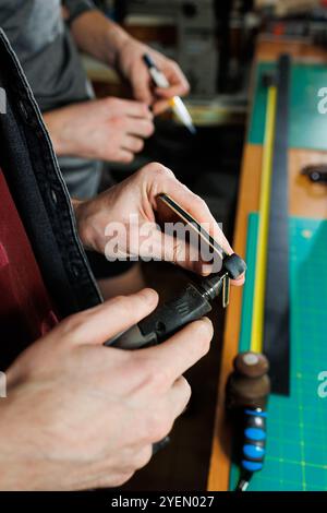 The hands of the master sew handmade leather products. Men's hands connect the parts, creating quality leather accessories. Working process in a leath Stock Photo