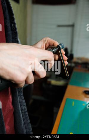 The hands of the master sew handmade leather products. Men's hands connect the parts, creating quality leather accessories. Working process in a leath Stock Photo