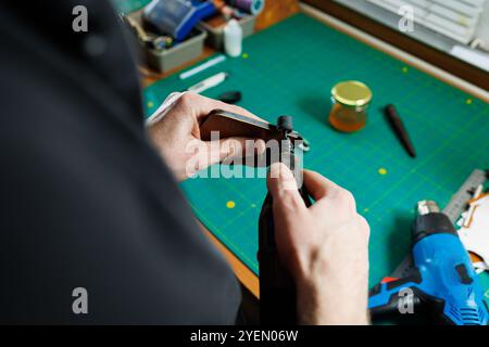 The hands of the master sew handmade leather products. Men's hands connect the parts, creating quality leather accessories. Working process in a leath Stock Photo