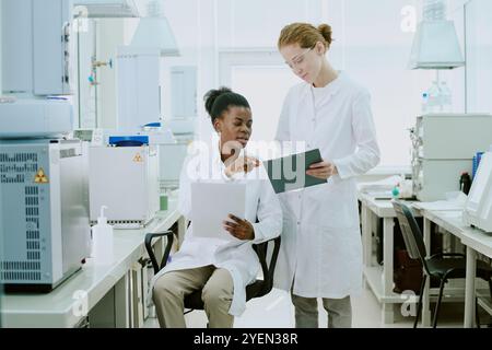 Two scientists engaged in research in modern laboratory, reviewing data and discussing findings. They are surrounded by advanced equipment, indicating high-tech environment Stock Photo