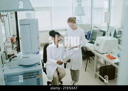 Scientists collaborating in laboratory environment, discussing research data while using advanced scientific equipment, fostering innovation and discovery in science Stock Photo