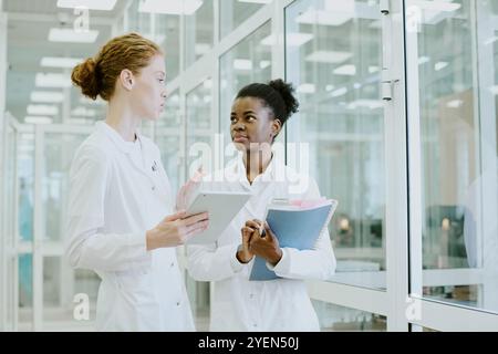 Two female scientists in laboratory coats discussing research data in modern laboratory, showing deep focus and engagement in their work Stock Photo
