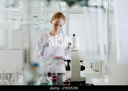 Scientist analyzing samples in bright, sterile laboratory wearing protective gear and gloves, surrounded by scientific equipment and instruments, focused on pipetting liquid Stock Photo