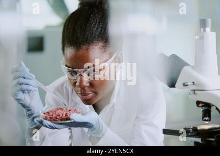 Scientist wearing protective gear analyzing tissue samples under microscope in laboratory environment with concentration and precision Stock Photo