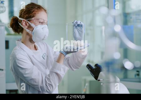 Researcher wearing protective gear and holding clear container with a laboratory mouse in scientific lab setting observing specimen with focused expression Stock Photo