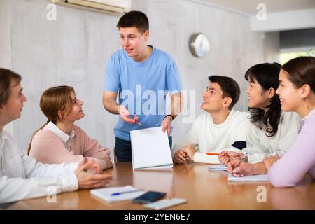Cheerful young student discussing learning assignment with coursemates Stock Photo