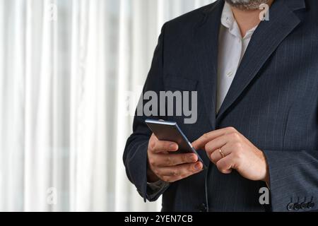Businessman in tailored suit using smartphone in modern office, focused on communication. Stock Photo