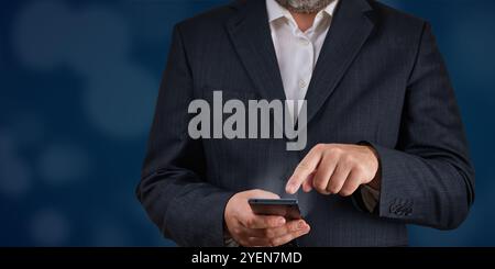 Businessman in suit holding and using smartphone with dark blue background Stock Photo