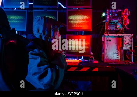 Woman hacker wear hood sit front computer typing on keyboard hacking servers in neon light, Gamer Stock Photo