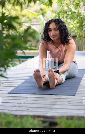 Woman stretching on yoga mat outdoors, enjoying peaceful exercise in nature. Fitness, wellness, meditation, mindfulness, relaxation, tranquility Stock Photo