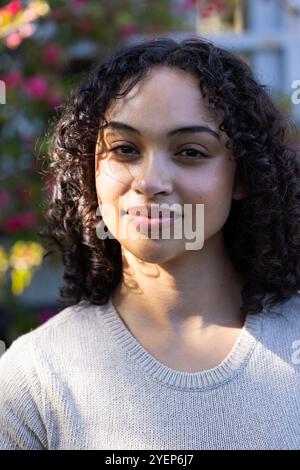 Smiling woman enjoying sunny day outdoors with blooming flowers in background. Nature, happiness, spring, floral, garden, sunshine Stock Photo