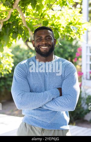Smiling African american man in blue sweater standing outdoors, enjoying sunny day. Portrait, happiness, cheerful, nature, sunlight, bright Stock Photo