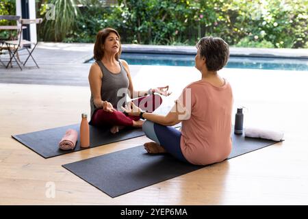 Senior female friends practicing yoga together by pool, enjoying peaceful outdoor session. Wellness, fitness, meditation, exercise, harmony, lifestyle Stock Photo