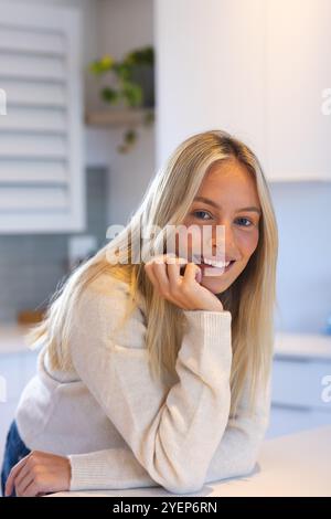 Smiling woman in cozy sweater leaning on kitchen counter at home. Lifestyle, happiness, comfort, relaxation, domestic, casual Stock Photo