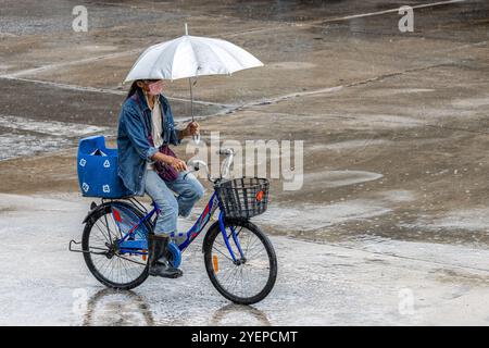 SAMUT PRAKAN, THAILAND, OCT 03 2024, A woman rides a bicycle with an umbrella in her hand Stock Photo