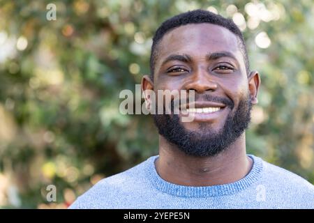 Smiling African american man enjoying outdoor autumn day, wearing cozy blue sweater, copy space. nature, season, weather, foliage, fashion Stock Photo