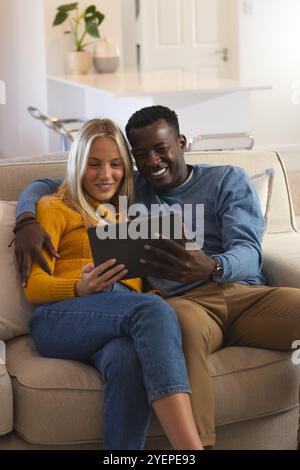 Happy multiracial couple relaxing on couch, enjoying tablet together at home. technology, leisure, cozy, bonding, digital, gadget Stock Photo